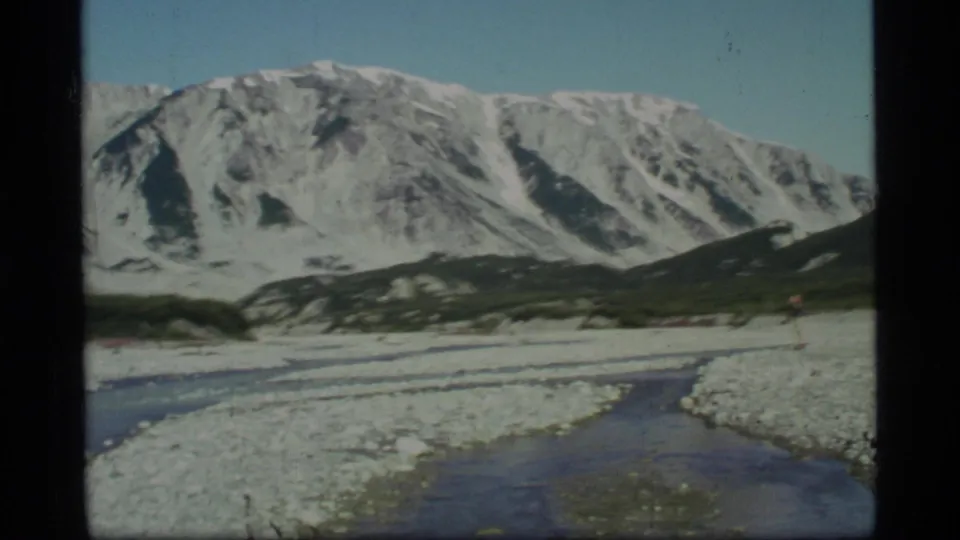 Glacier Bay 8mm landscape frame with a winding stream crossing a gravel riverbed below broad snow-covered mountains.