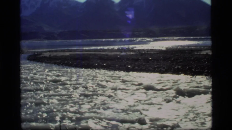 Glacier Bay river bend on 8mm film, with foaming current, rocky bank, and dark mountains beyond.