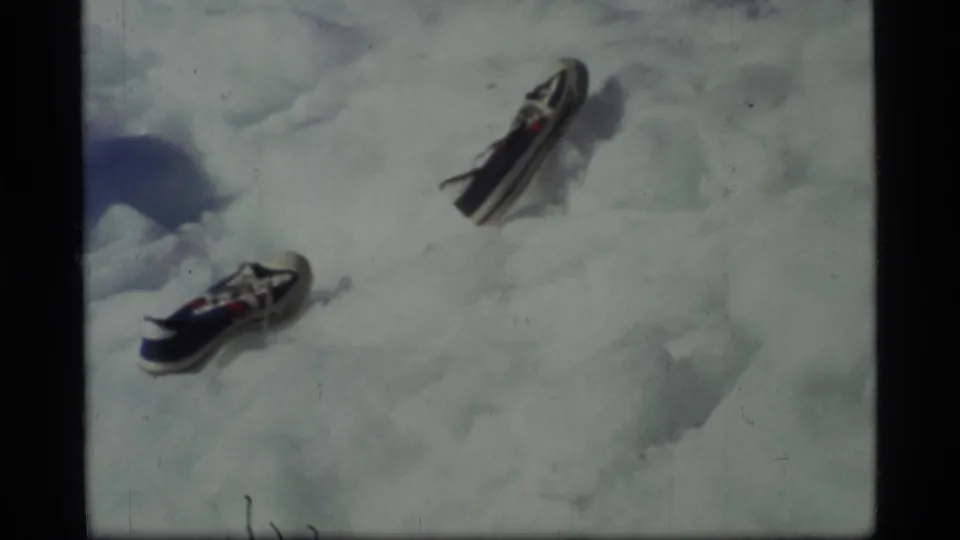 1977 Glacier Bay home-movie frame showing two sneakers placed apart on uneven snow or ice.