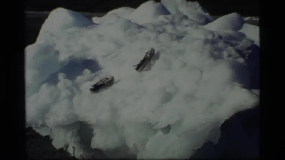 1977 Glacier Bay 8mm frame showing a large irregular iceberg on shore with two dark objects lodged on its surface.