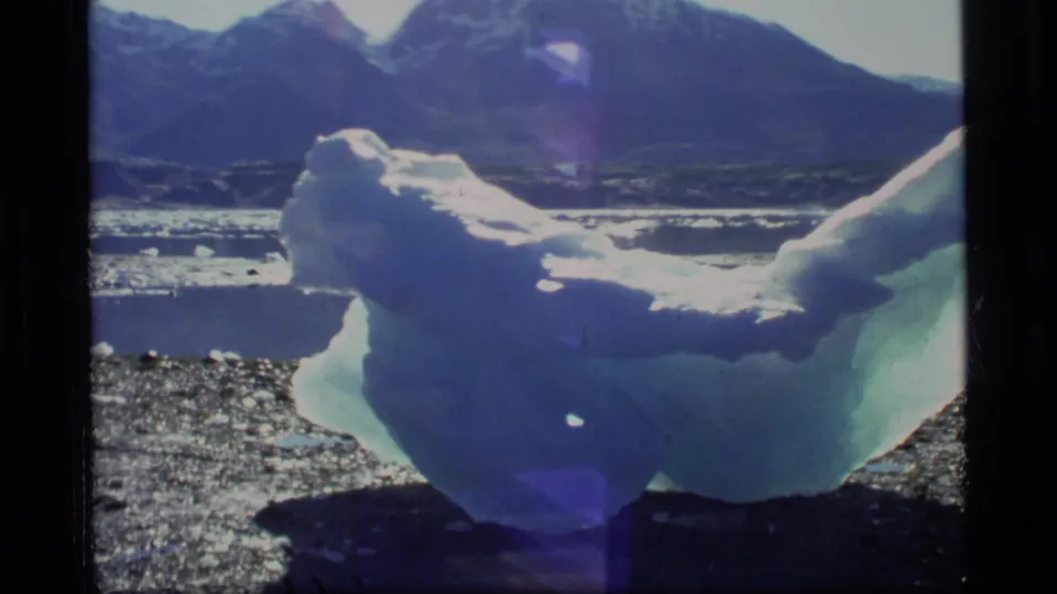 A wider 8mm view shows the iceberg from the side in Glacier Bay, with reflective water and mountains behind it.