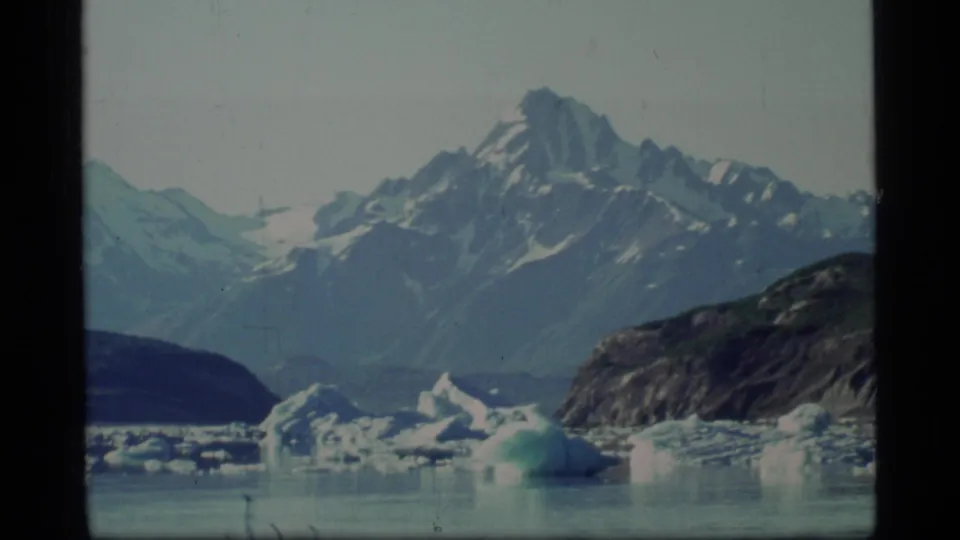 Glacier Bay, Alaska, shown on 8mm film with icebergs, still water, snow-streaked mountains, and a rocky shore.
