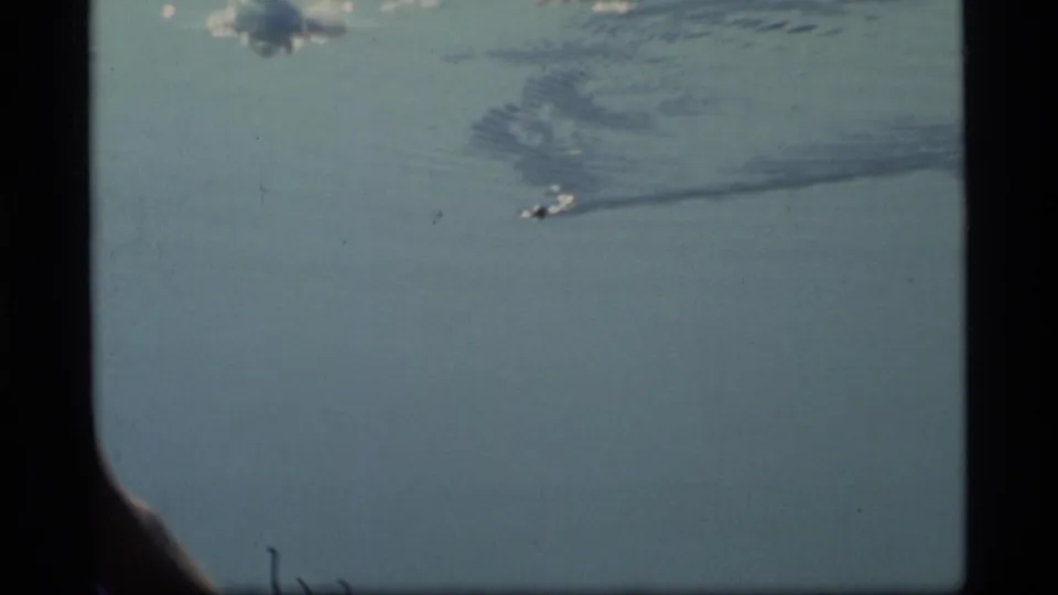 Glacier Bay home-movie view of a small boat crossing pale blue water, its wake spreading behind it within the 8mm frame.