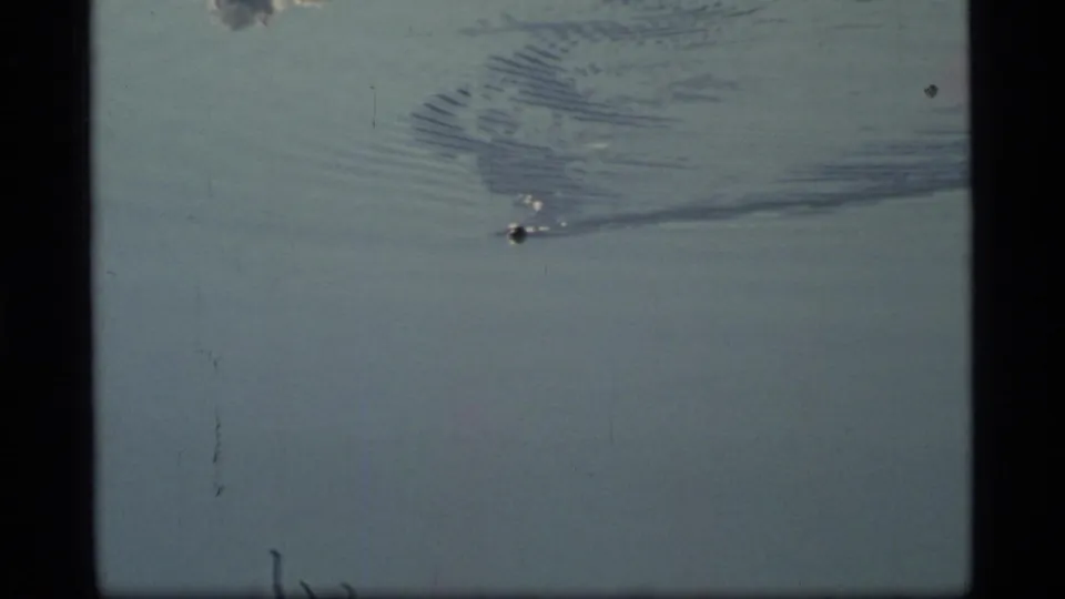 1977 Glacier Bay frame showing a small boat on calm water with a broad rippling wake and visible 8mm film borders.