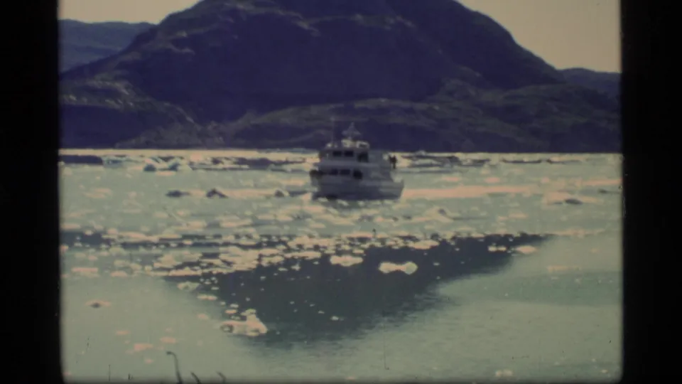 1977 Glacier Bay 8mm frame showing a small boat among ice floes with rugged mountains behind it.