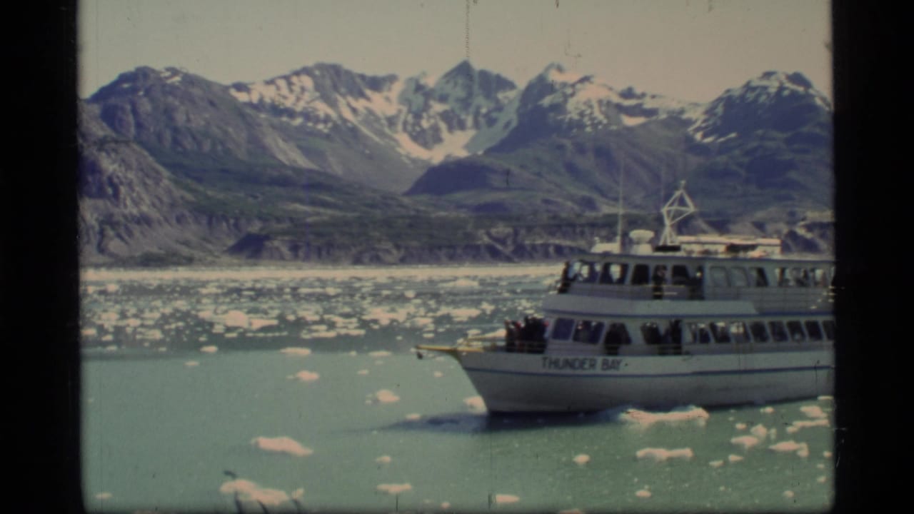 Thunder Bay tour boat at right with passengers, ice floes, and snow-capped mountains.