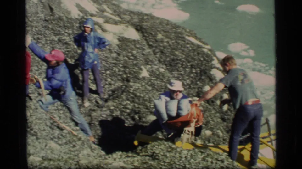 1977 Glacier Bay home-movie view of workers or passengers moving bags on a rocky landing beside the boat and icy water.