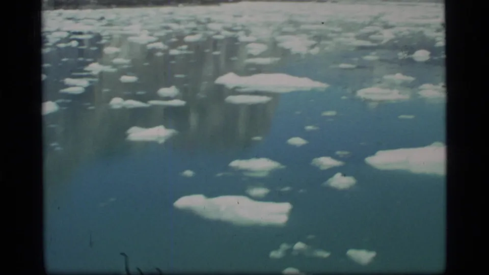 Vintage 8mm Glacier Bay frame with numerous small ice pieces spread across blue-green water from a moving vessel.