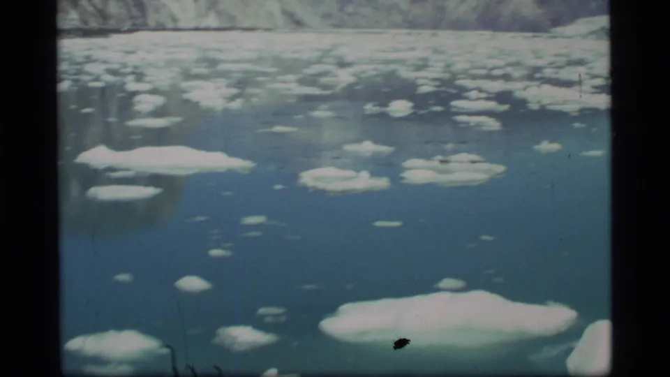 1977 8mm view in Glacier Bay showing floating ice across the water and a soft distant glacier or shoreline form.