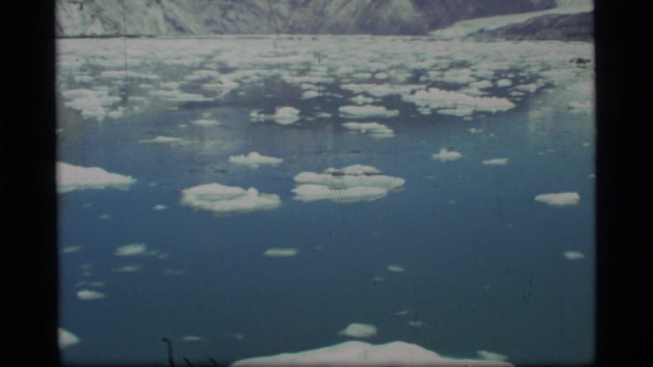 1977 8mm Glacier Bay view of blue water dotted with ice floes and a distant mountainous shore.