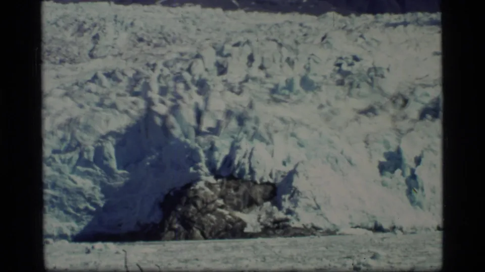 Glacier Bay, Alaska, 1977, showing a wide glacial wall with rugged ice texture and a dark rock outcrop near the water.