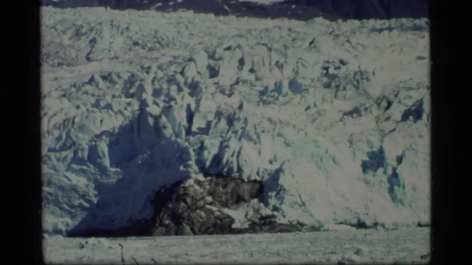 1977 Glacier Bay home-movie frame showing a glacier front, blue shadowed ice, dark rock, and compacted snow textures.