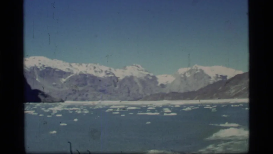 Glacier Bay, Alaska view from a boat, showing scattered ice floes across blue water and a broad snow-covered mountain range.