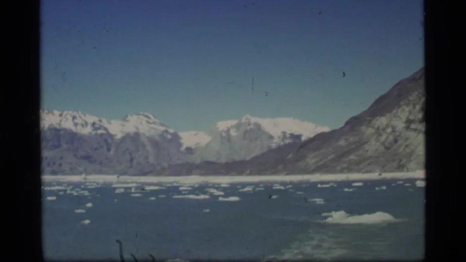 Boat passenger view in Glacier Bay with wake in the foreground, scattered ice, mountain shoreline, and pale glacier-like ice in the distance.