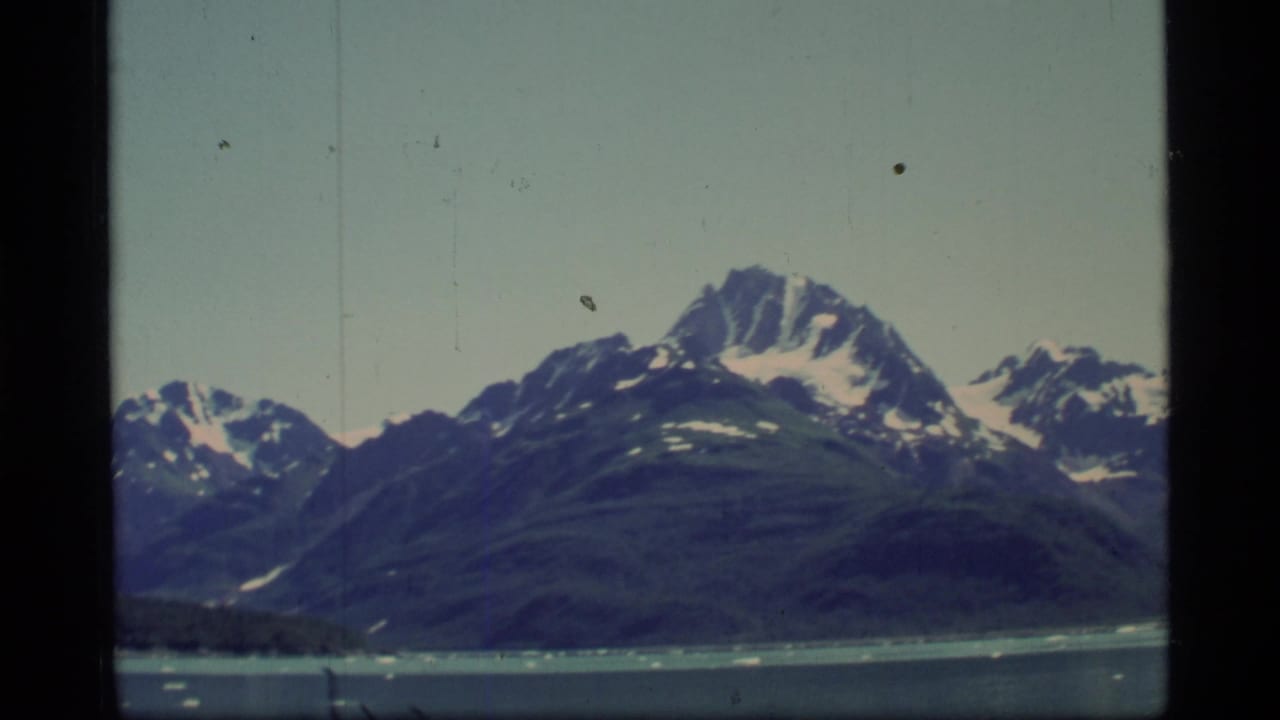 Snow-covered mountain range above icy water under a pale sky.