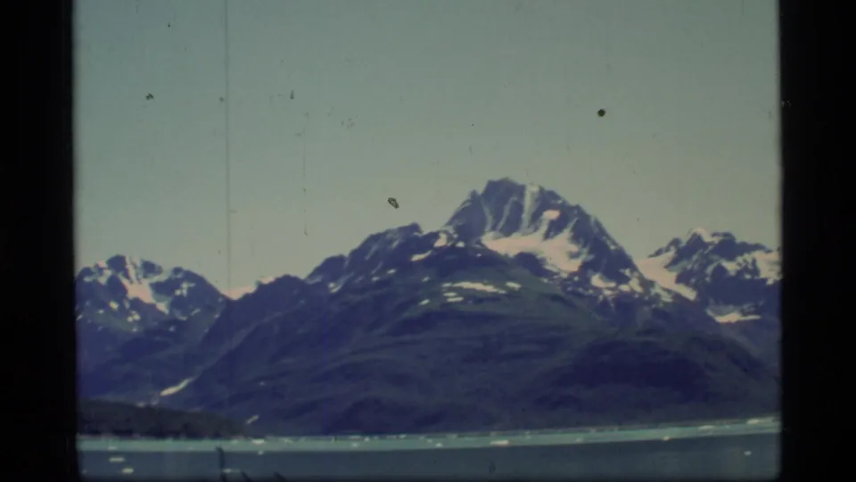 1977 Glacier Bay, Alaska 8mm frame showing snow-streaked mountains beyond cold water and small ice pieces.