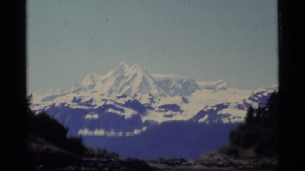 Snow-capped mountain above dark shoreline with pale sky and 8mm frame edges.