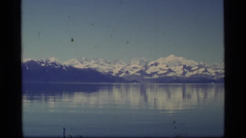 Glacier Bay landscape on 8mm film, with a broad snow-covered mountain range mirrored in quiet water.