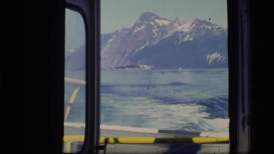 1977 Glacier Bay view from inside a moving boat, showing wake trails on the water and high mountains across the fjord.