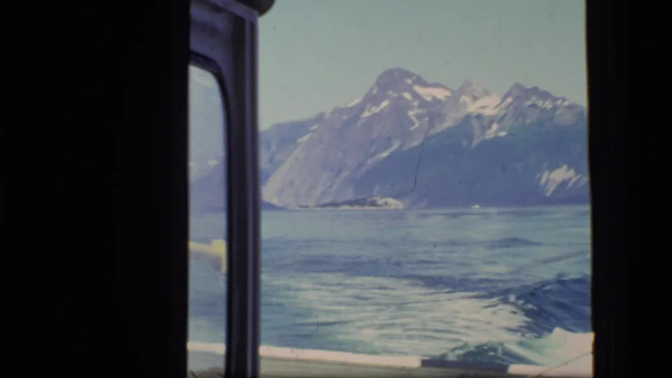 Home-movie view from a boat in Glacier Bay, with mountains, reflective water, and the vessel wake seen through the window.