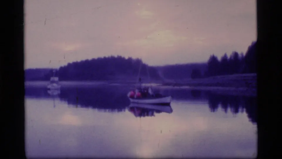 Dusk scene in the 1977 Alaska home movie showing a small boat on still water, with treeline and colored sky reflections.