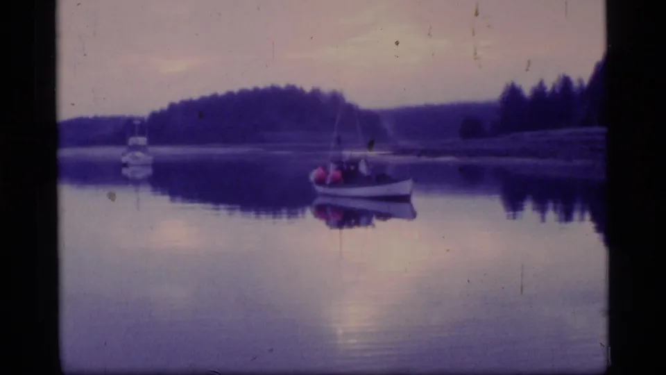 1977 8mm Glacier Bay view of a small boat with occupants on still water beneath a purple dusk sky.
