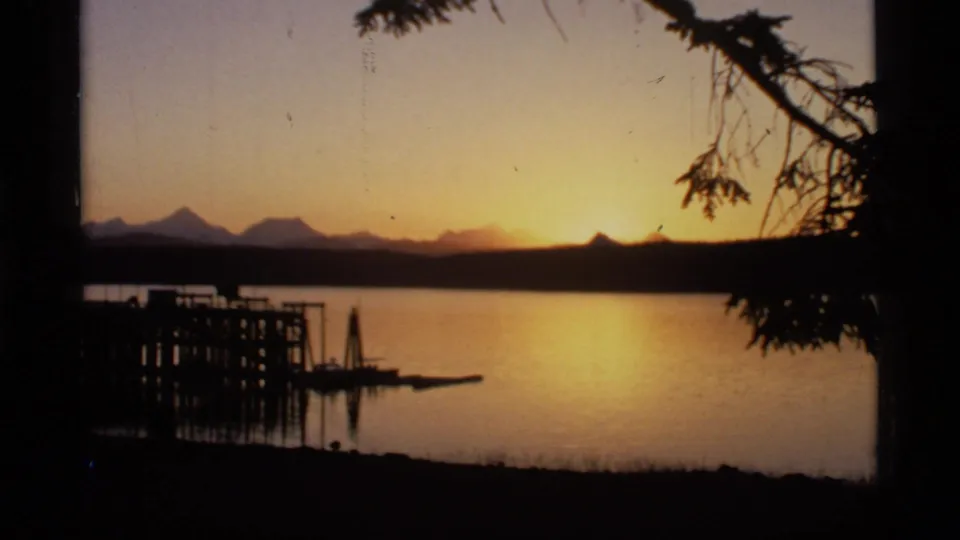 Glacier Bay sunset scene on 8mm film, showing amber light over water with a pier and mountain silhouettes.