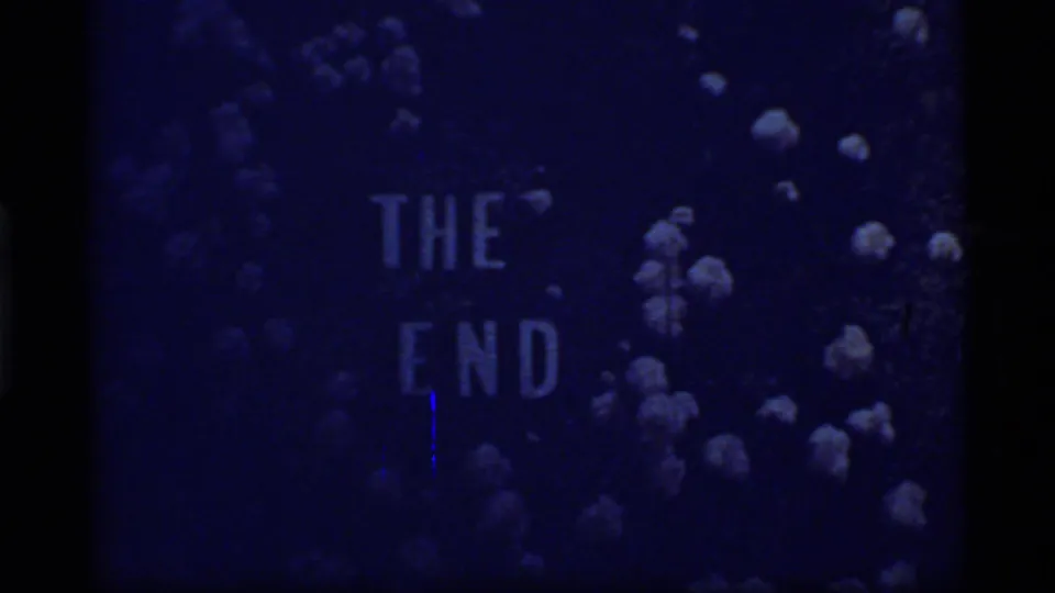 Dim 1977 8mm frame showing THE END on a blue floral background, partially obscured by low exposure.
