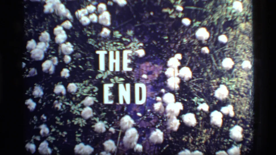 Final 1977 8mm frame shows a bright floral THE END card with white blossoms, greenery, and visible small-gauge film texture.