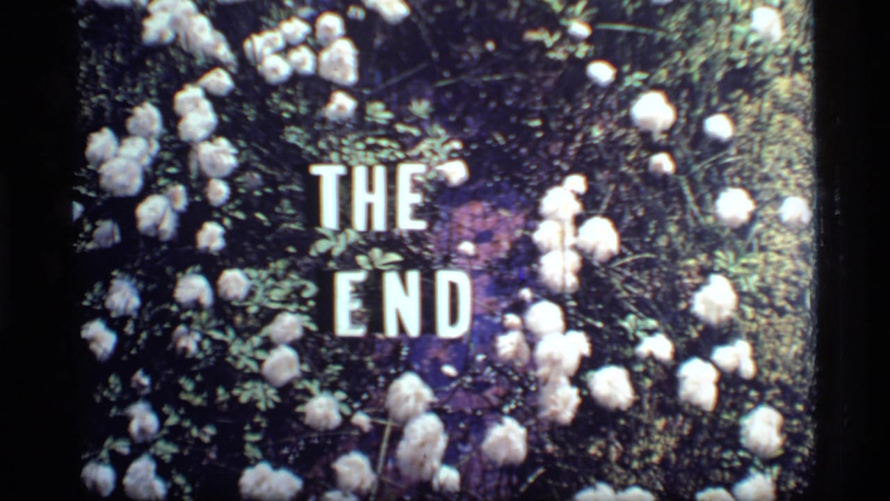 1977 8mm home-movie frame with white THE END lettering set among white flowers and dark foliage.