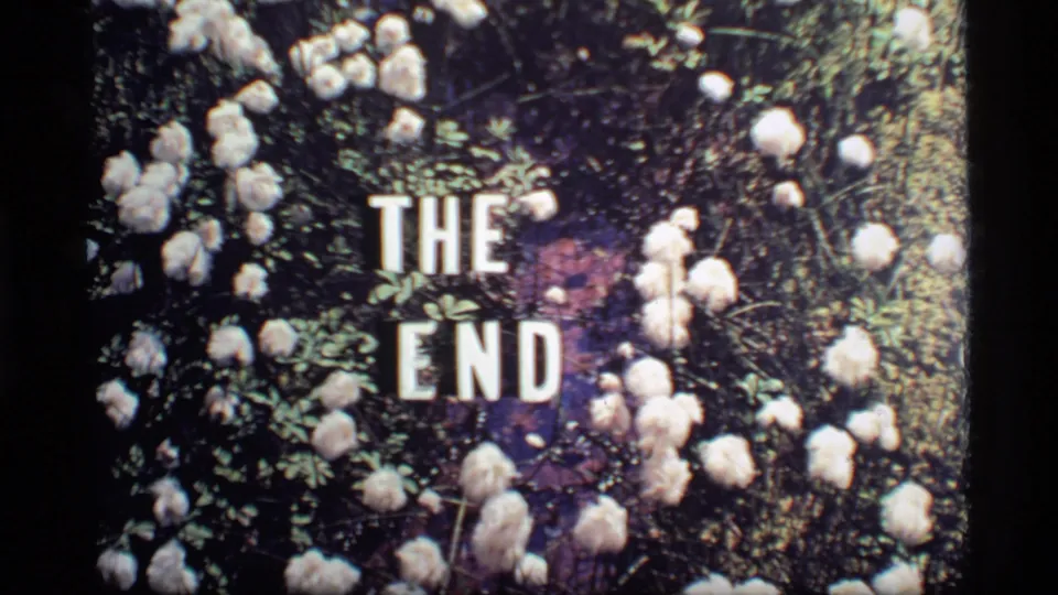 Glacier Bay 1977 reel ending frame showing bold white THE END text surrounded by pale flowers and greenery.