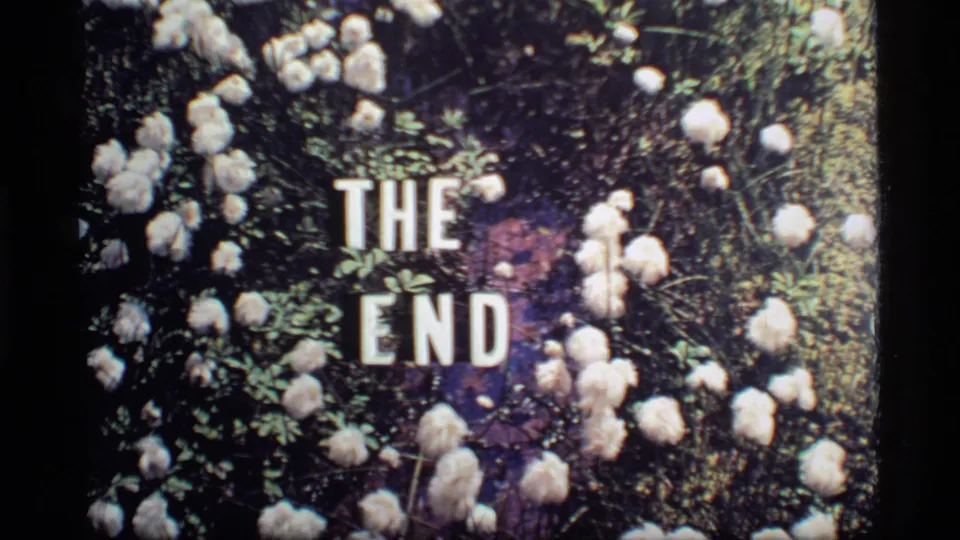 Final 1977 8mm frame showing THE END in white block letters over a dark floral arrangement.