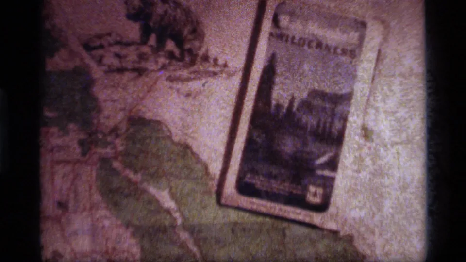 1977 8mm frame of a wilderness brochure lying diagonally across a National Forest map for Sapphire Lake, Montana travel planning.
