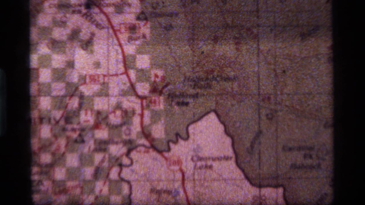 1977 8mm Montana home-movie frame showing a paper map with red marked routes and partially legible place names.