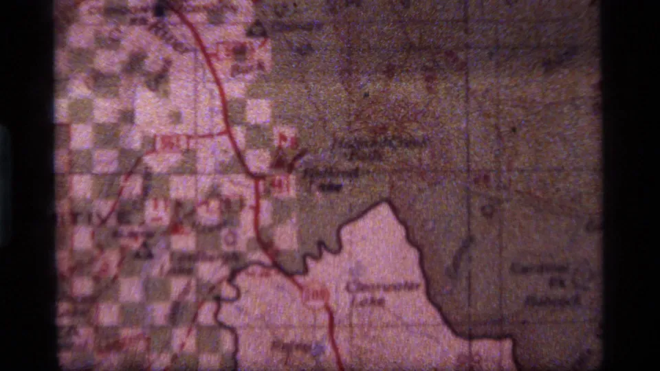 1977 8mm Montana home-movie frame showing a paper map with red marked routes and partially legible place names.