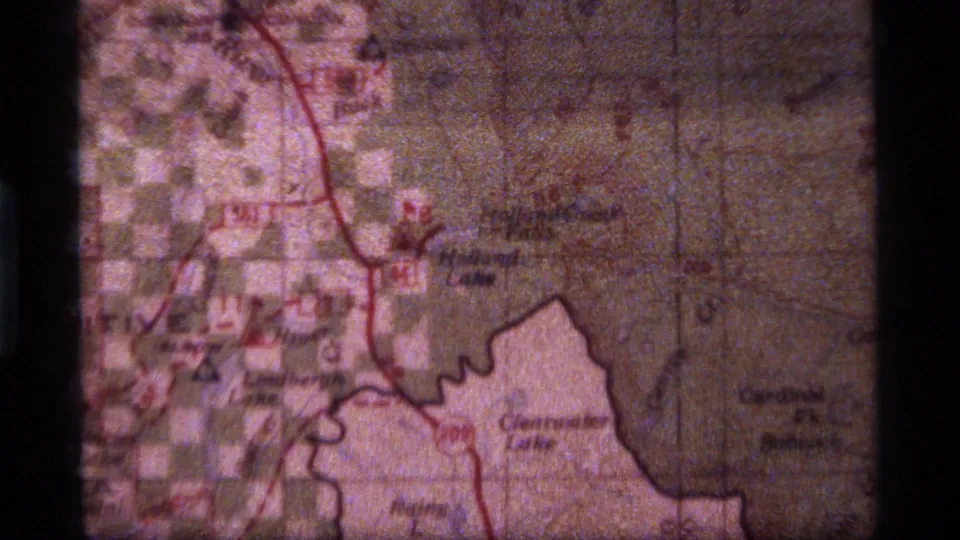 Close 8mm frame of a Montana-area map with red route lines and faded, grainy color from the supplied 1977 clip.