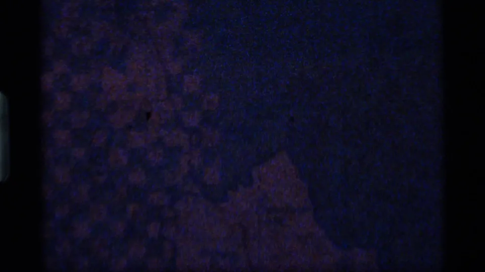 Underexposed 8mm frame from the 1977 Montana clip, with blue cast and indistinct map or sign detail.