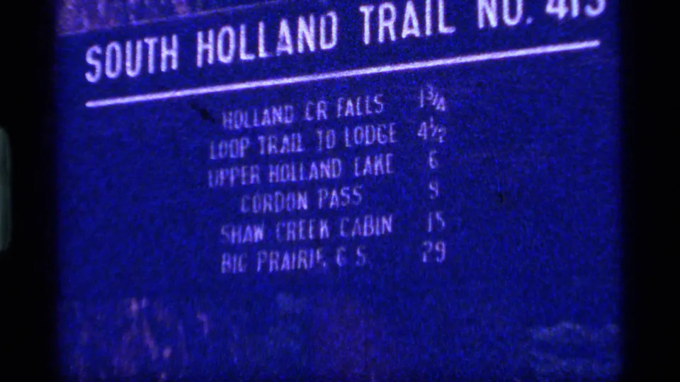 1977 8mm Montana frame showing a blue South Holland Trail sign with white mileage text for nearby trail destinations.