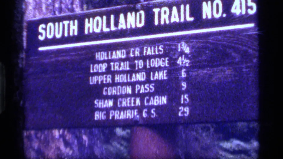 Blue-shifted 8mm frame of a South Holland Trail No. 413 sign, with destinations and mileages readable in part.