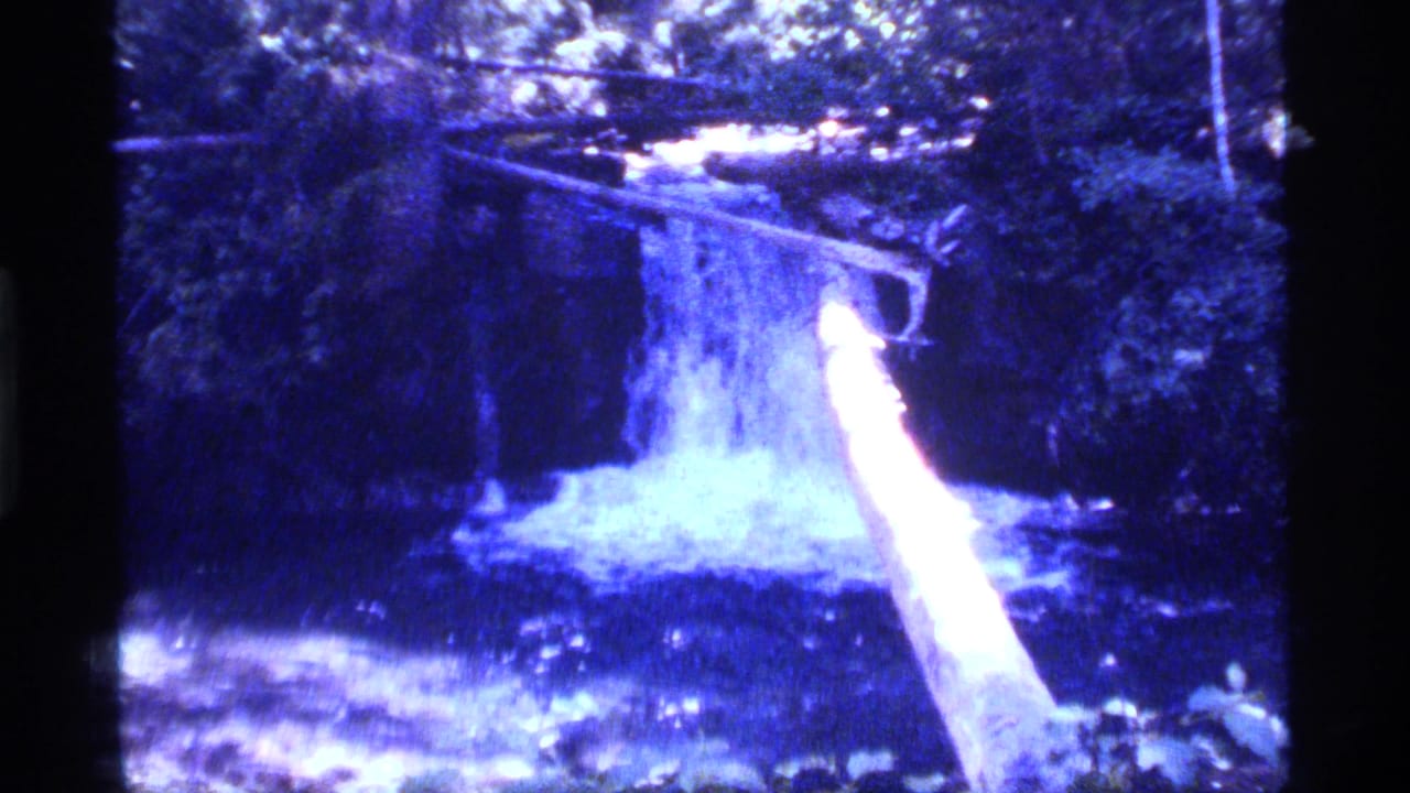 1977 8mm view at Sapphire Lake, Montana, showing a small waterfall, bright fallen log, and dense streamside foliage.