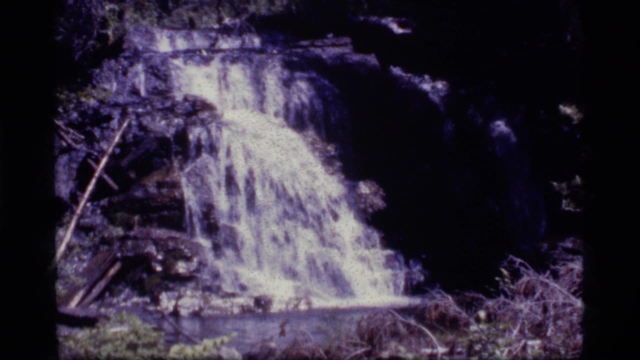 Waterfall cascading over rocky ledges in a shaded forest setting.