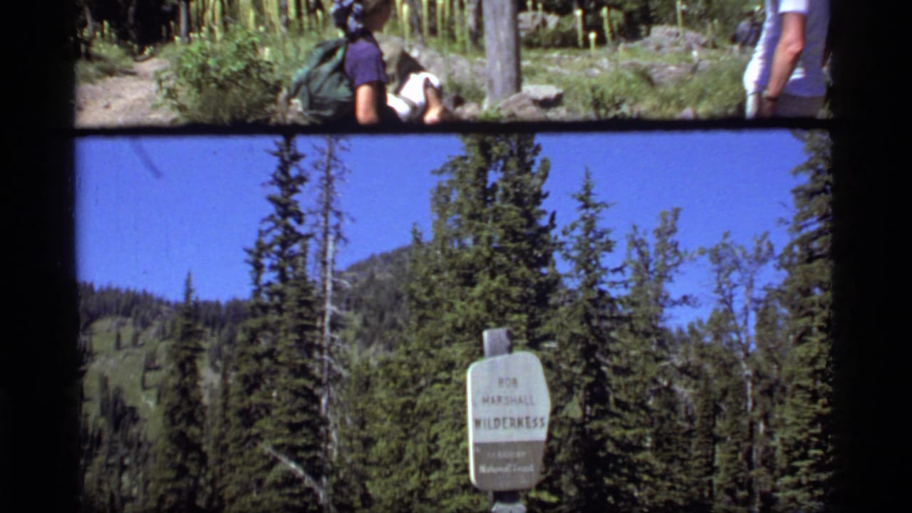 1977 Montana 8mm frame showing a Bob Marshall Wilderness sign in forested mountain terrain near Sapphire Lake.