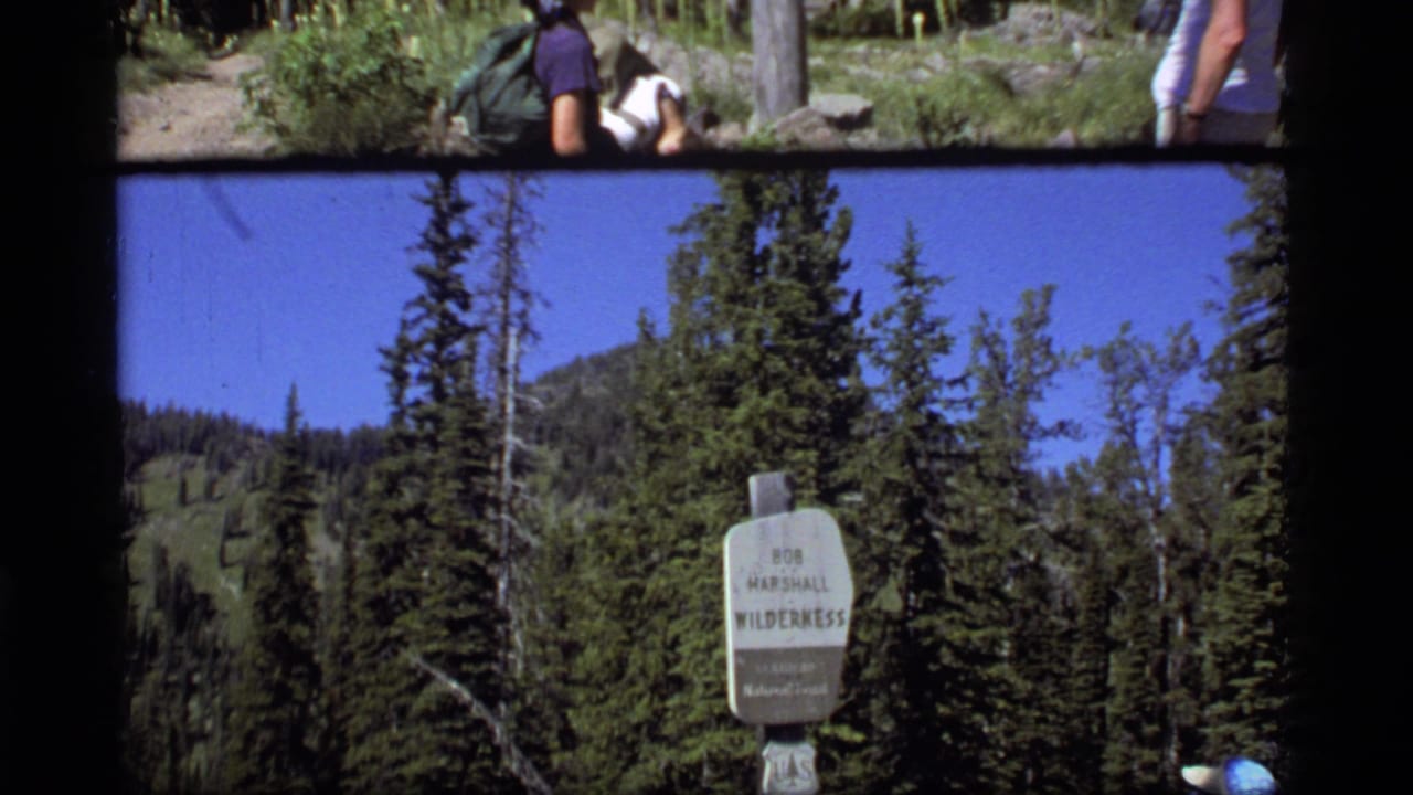 1977 Montana home-movie frame with the Bob Marshall Wilderness sign and a partial hiker at the right edge.