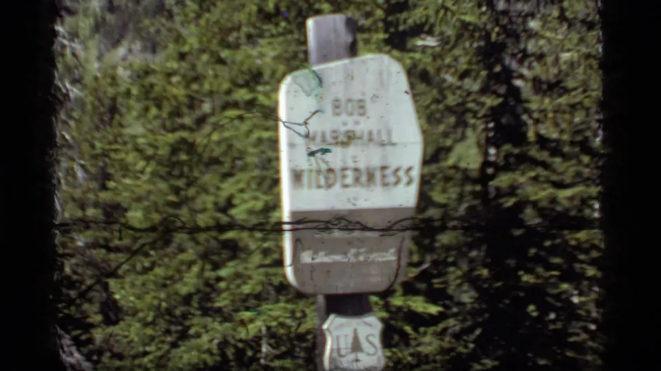 A softer 8mm frame shows the Bob Marshall Wilderness sign partially obscured by film wear and surrounding forest.