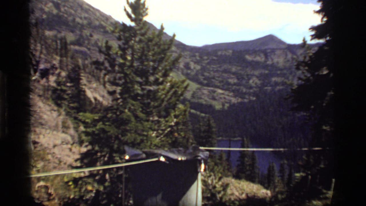 1977 8mm view from a Sapphire Lake, Montana campsite, with evergreens, a mountain lake, and a rope or clothesline in front.