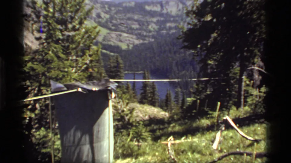 A 1977 Sapphire Lake campsite view shows rope or clothesline, shelter fabric, evergreens, and the lake below forested slopes.