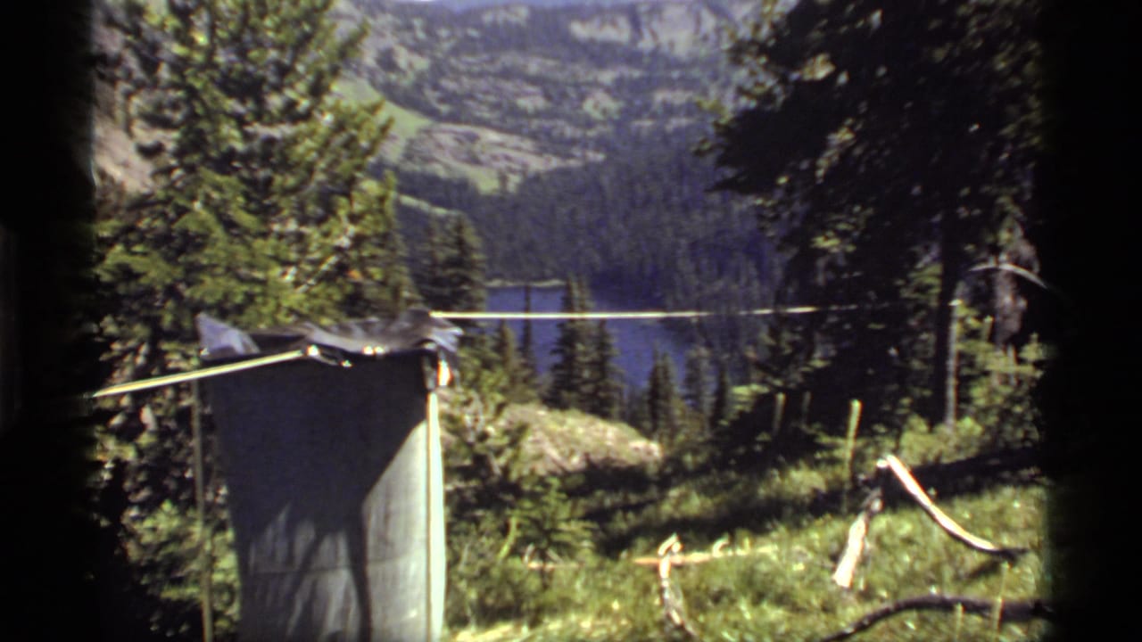 Mountain lake partly seen through trees with a small camp structure in the foreground.