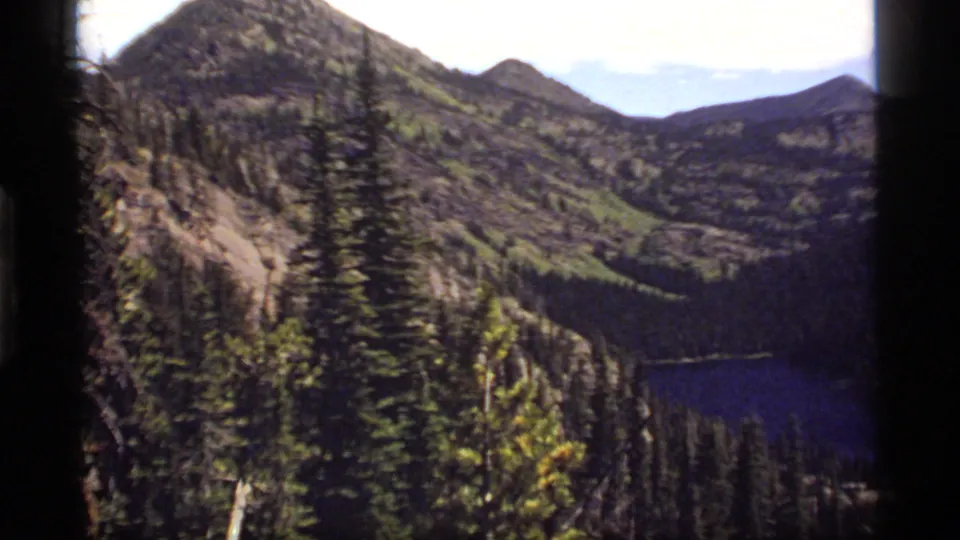 Sapphire Lake, Montana, appears below conifer forest and rocky alpine slopes in this 1977 8mm home-movie frame.