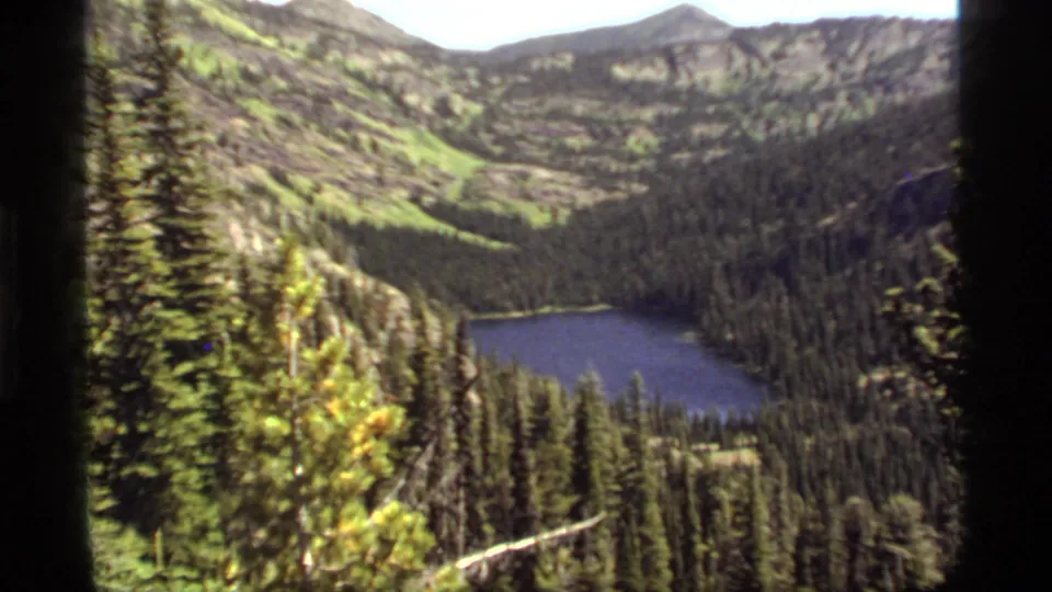 Sapphire Lake, Montana, appears below a wooded overlook in this 1977 8mm frame with soft grain and bright mountain light.