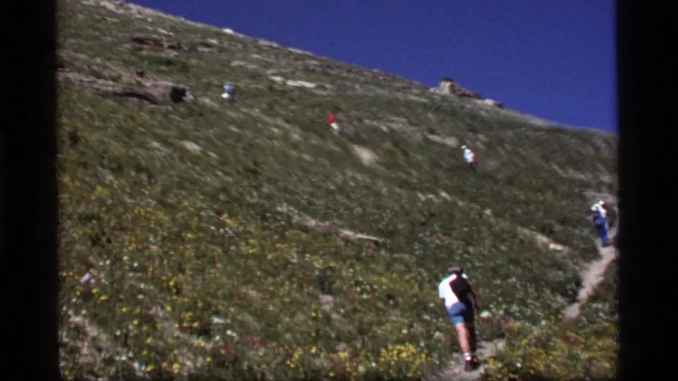 A close foreground hiker follows others up a steep switchback trail in 1977 Sapphire Lake, Montana home-movie footage.